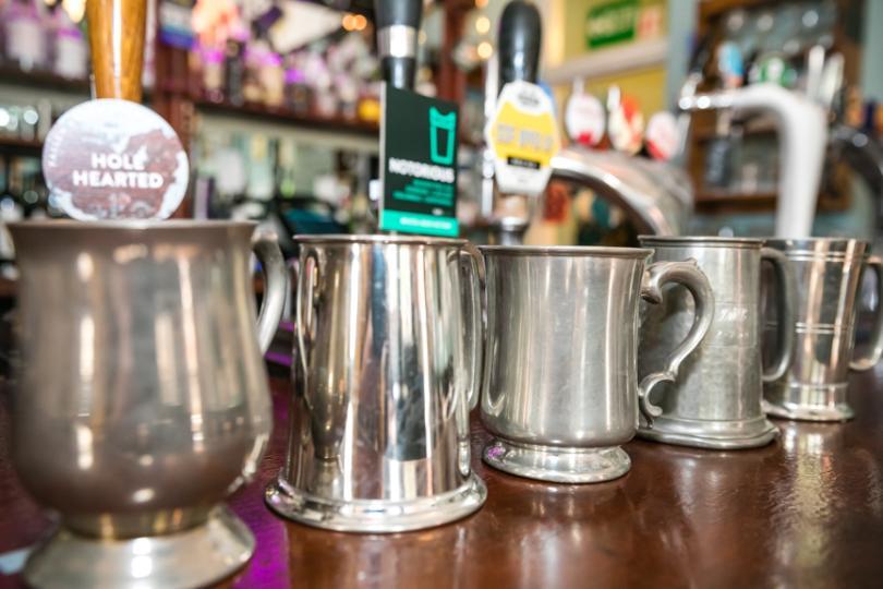 Pewter tankards on a bar top with handpulls behind