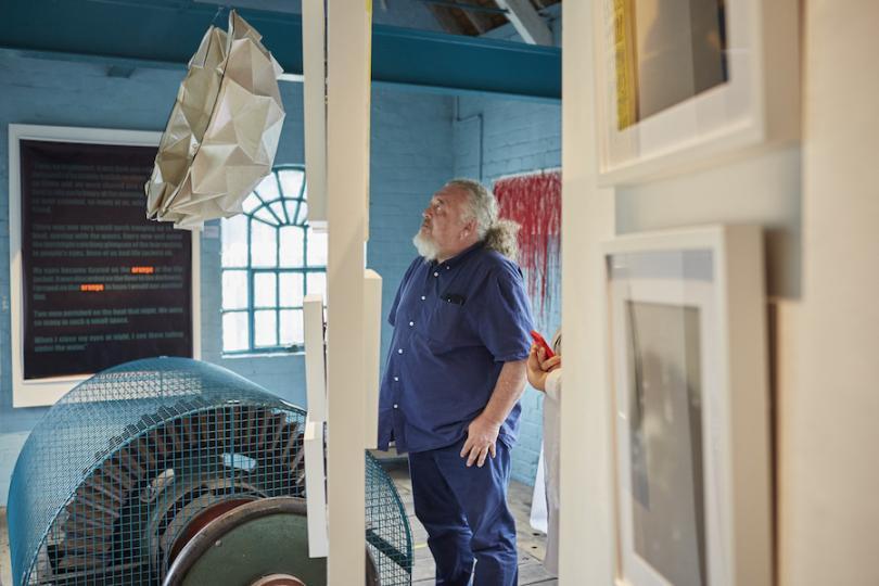 man in blue shirt looking up at white abstract sculpture hanging 