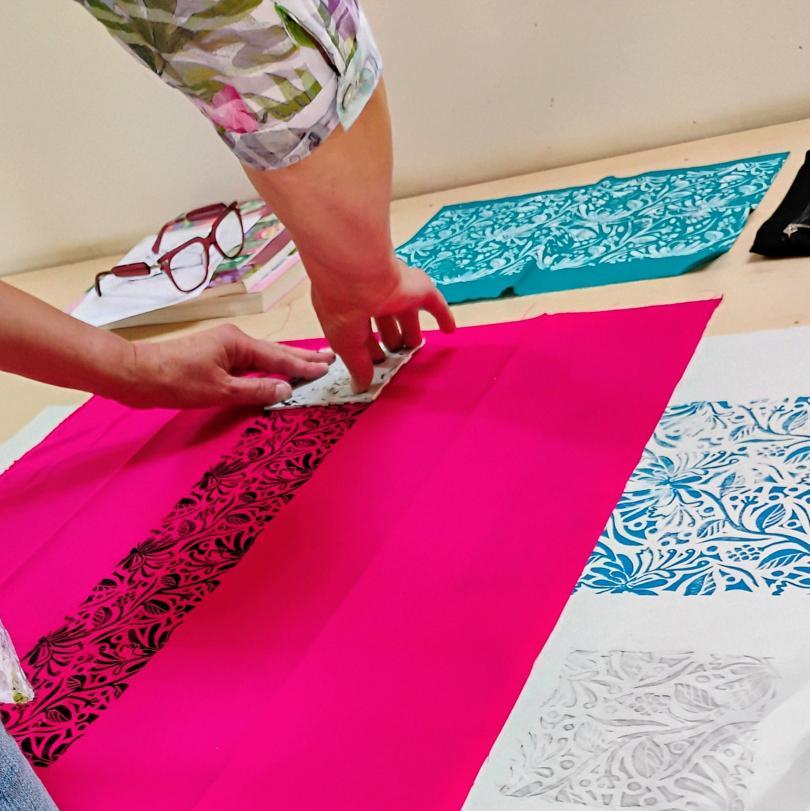 Woman printing onto pink fabric using a stamp