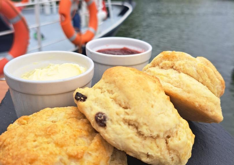 Scones with Clotted Cream, and Jam on a serving slate with river and part of boat view