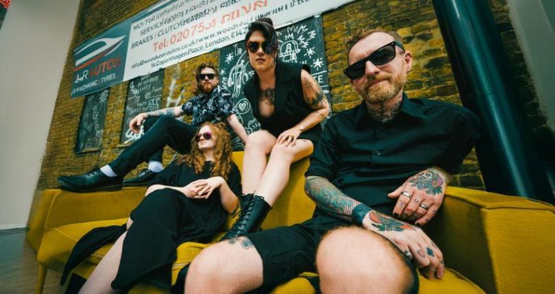 Millie Manders and The Shutup sitting on a sofa outside a mechanic's