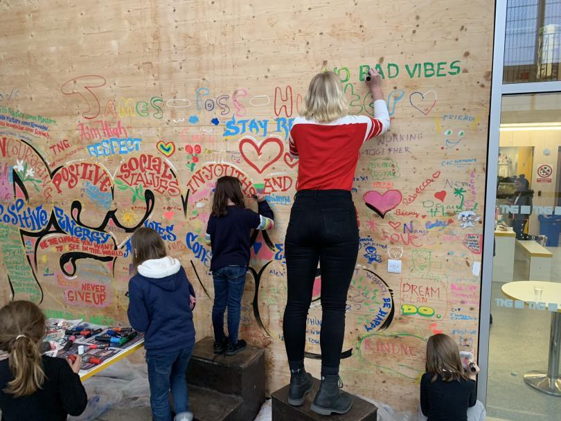 Image of a woman and two children with their backs to us decorating a wall for Fun Palaces