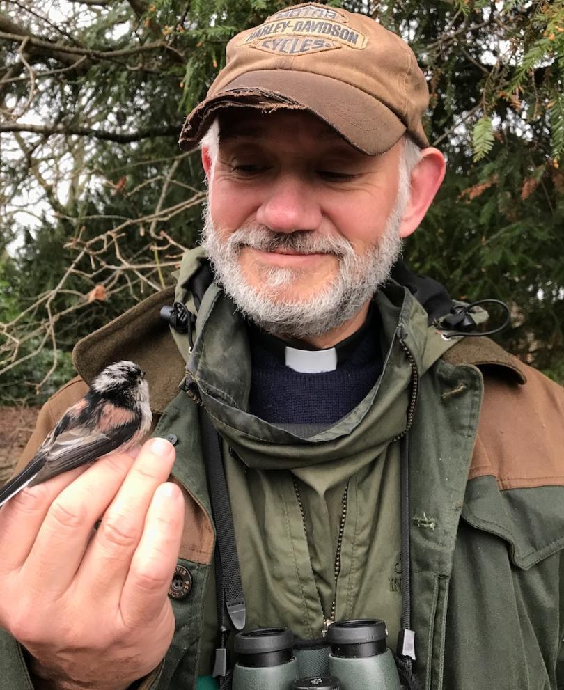 Andy Gosler in birding gear and clerical dog-collar holding a Long-tailed Tit