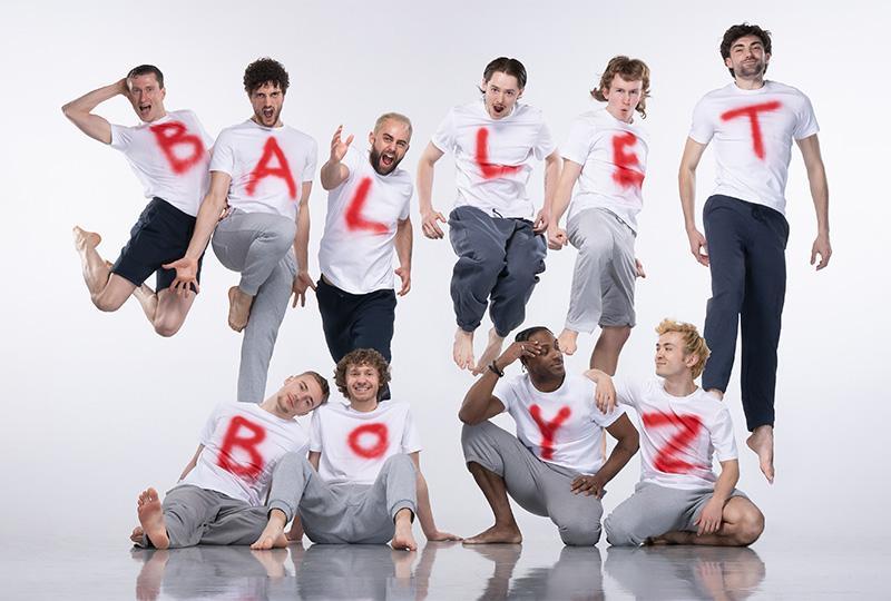 Photo of the Ballet Boyz wearing white t-shirts and dark trousers with red letters spraypainted on them. They're standing in a group so their shirts spell out Ballet Boyz.