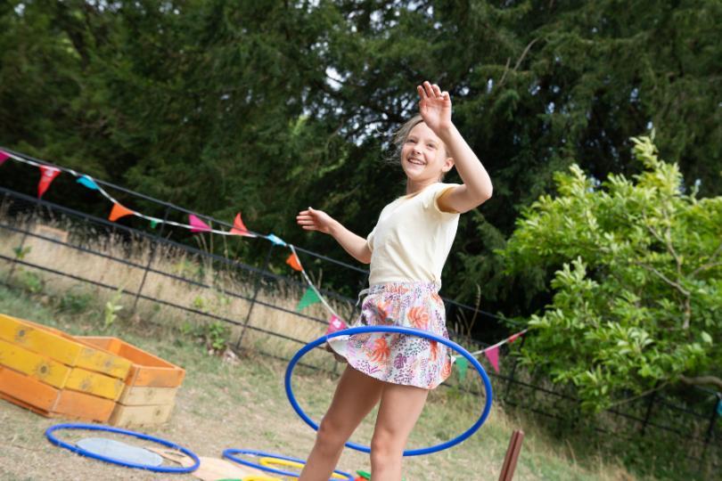 A young girl enjoying Summer of Play at Basildon Park. She is hoola hooping against a backdrop of parkland and bunting is hung along the play area.
