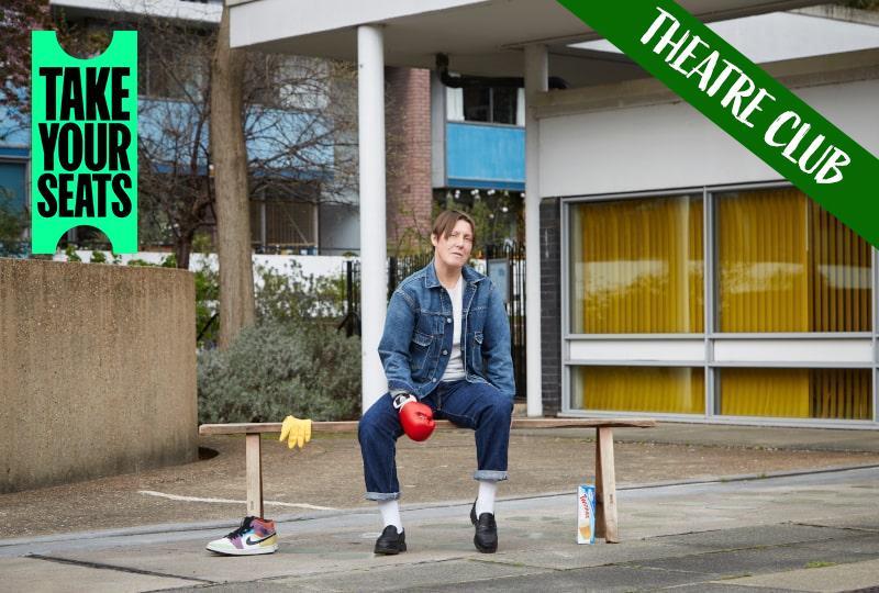 Photograph of Tink Flaherety sitting on a bench outside some office buildings. White text reading 'Theatre Club' is overlaid across the top right corner and the 'Take Your Seats' logo is in the top left corner
