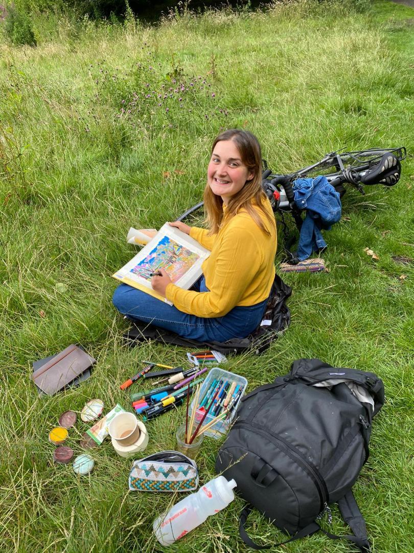 Christabel Forbes sat down on grass captured mid drawing 