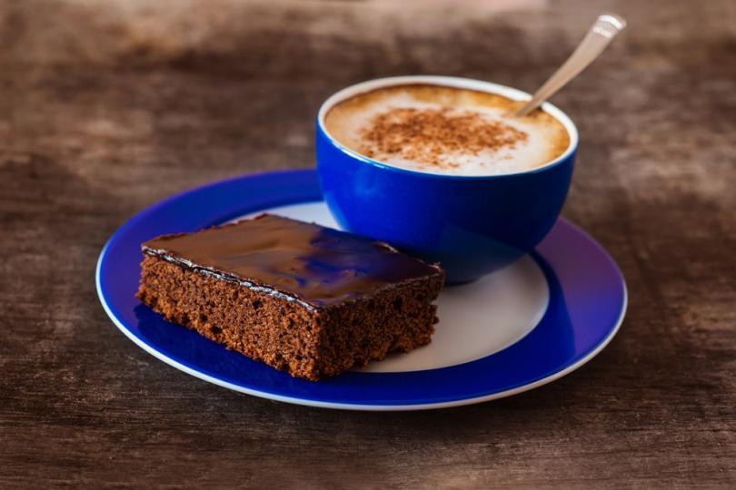 Blue cup and saucer. Coffee in cup and a chocolate brownie on the saucer beside cup.