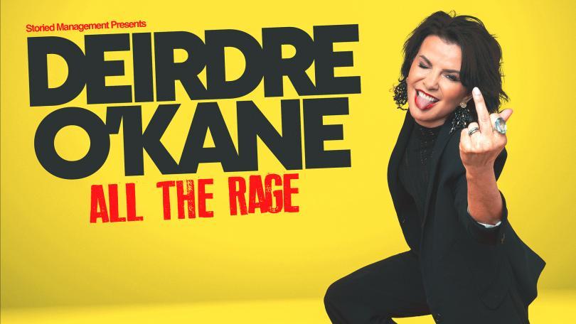Deirdre O'Kane on a yellow background, smiling and holding up middle finger. 