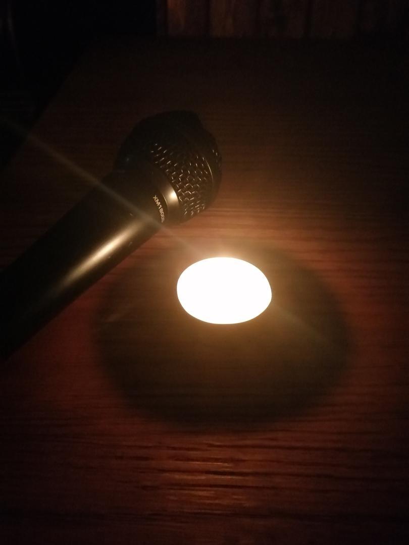 Picture of a tealight candle on a wooden table with a microphone beside it