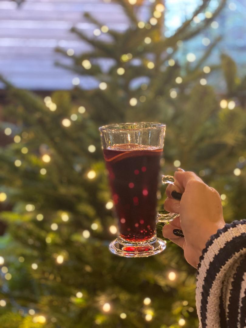 glass of mulled wine with christmas tree and lights behind