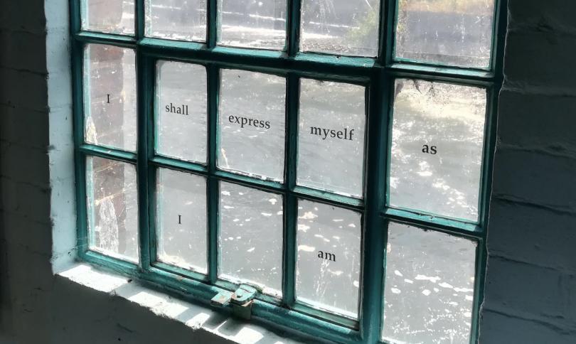 Photo of a blue painted window with ultiple panes of glass, displayed on the different panes are the words ' I shall express myself as I am'.
