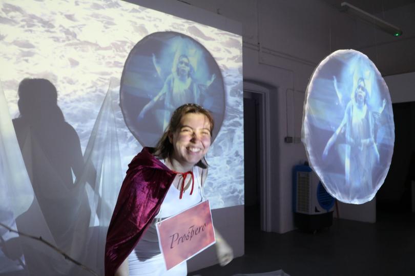 artist wearing red cape in front of projection of their work