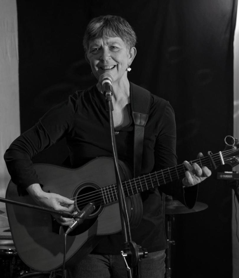 Black and white photograph of Maggie Holland singing and playing guitar