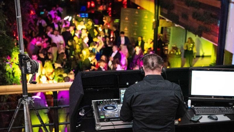 The image shows a DJ playing to a group of people on the dancefloor below.