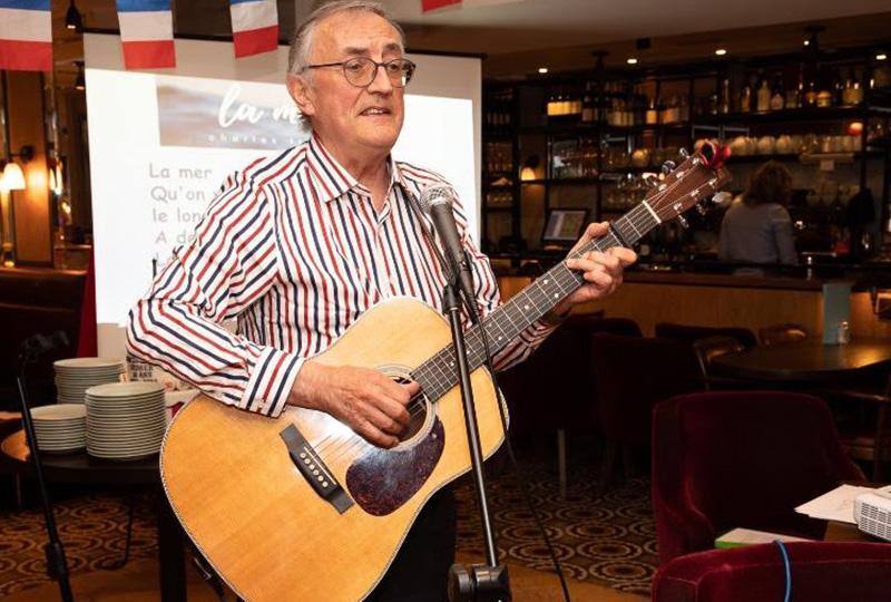 Musician Peter Prowse in a stiped shirt holding an acoustic guitar