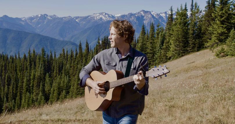 musician Scott Clay stood with a guitar in the mountains