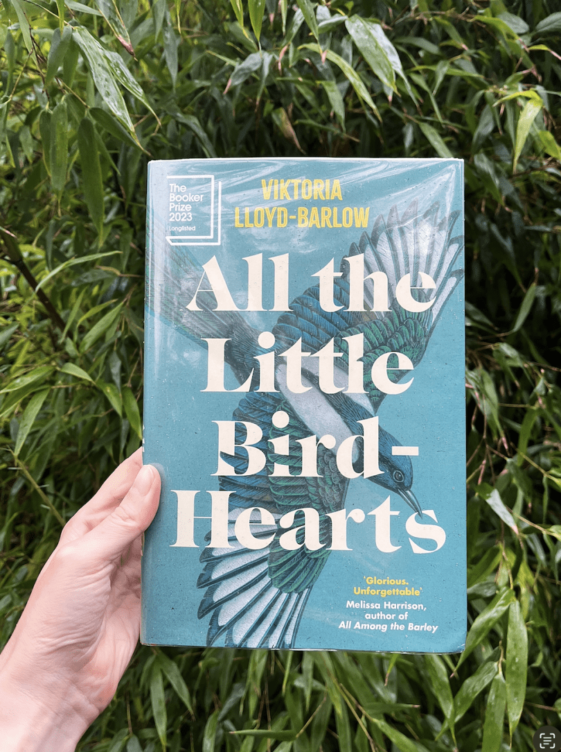 book titled all the little bird hearts held up in front of green plants