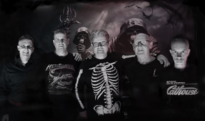 The band Vampire Strikers, five middle-aged men wearing black. The one in the middle has a skeleton printed on his jumper.