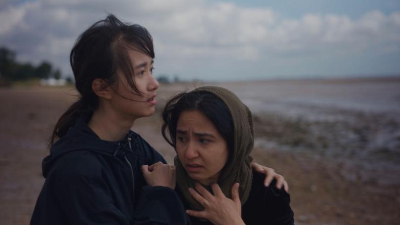 Two young female Hong Kongers huddling together against the windy, grey UK weather
