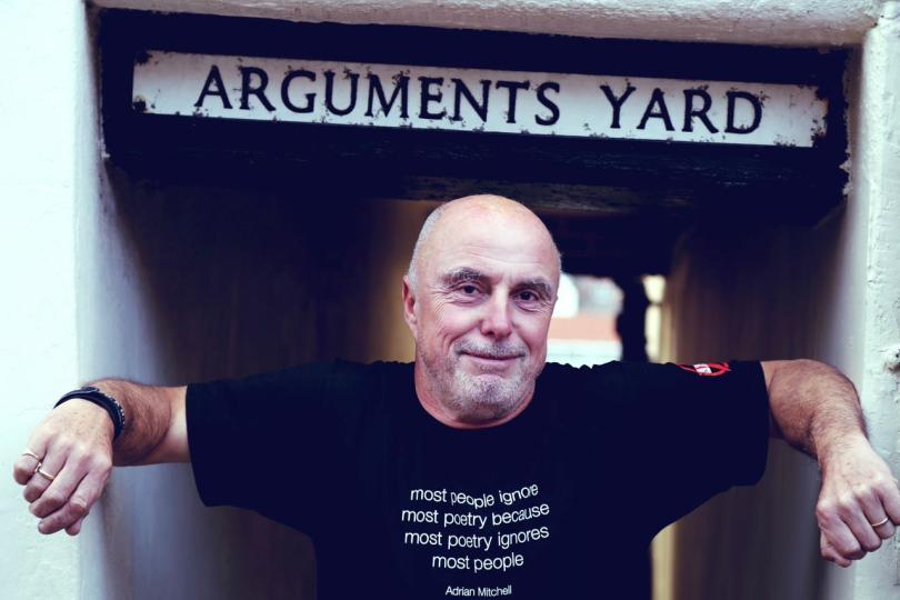 Attila The Stockbroker standing under a street sign saying "Arguments Yard"