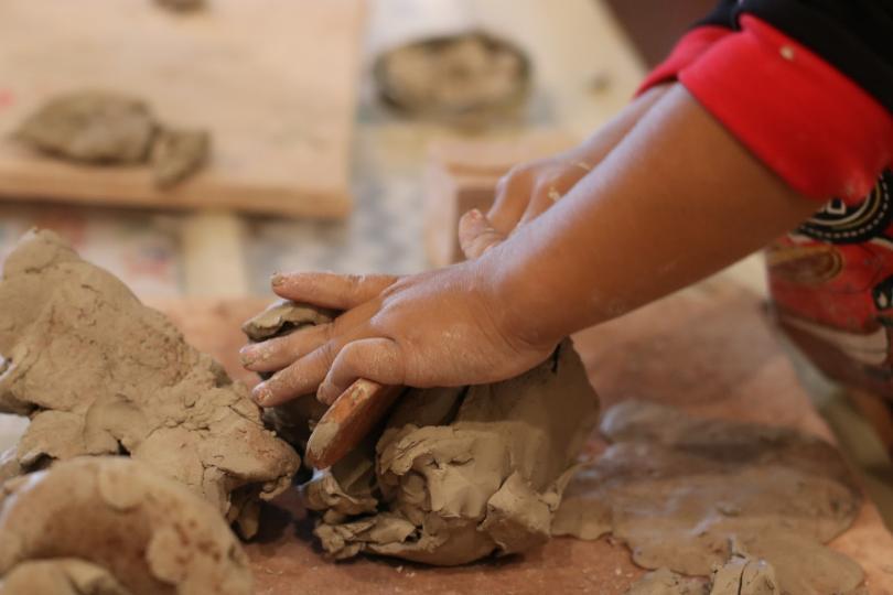 Image of a child's arm and hand kneading clay on a table. 