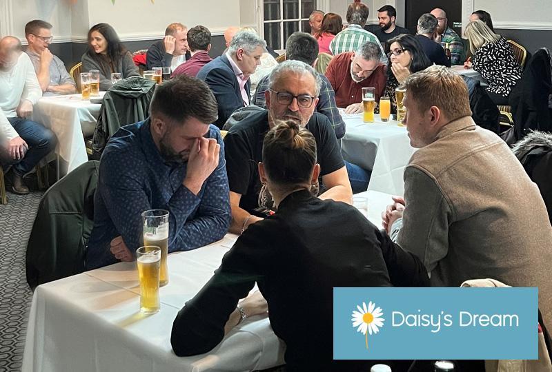 room full of people doing a quiz. Groups of 4-5 people sat around tables conferring.