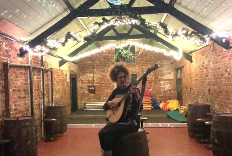 image of singer with a mandola sitting on a beer barrell in a brighlty lit room