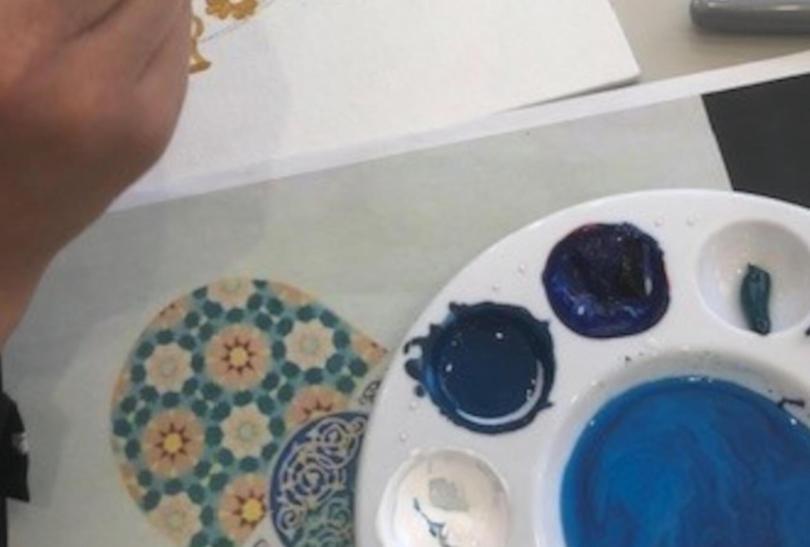 close up of a hand painting, next to a paint palette
