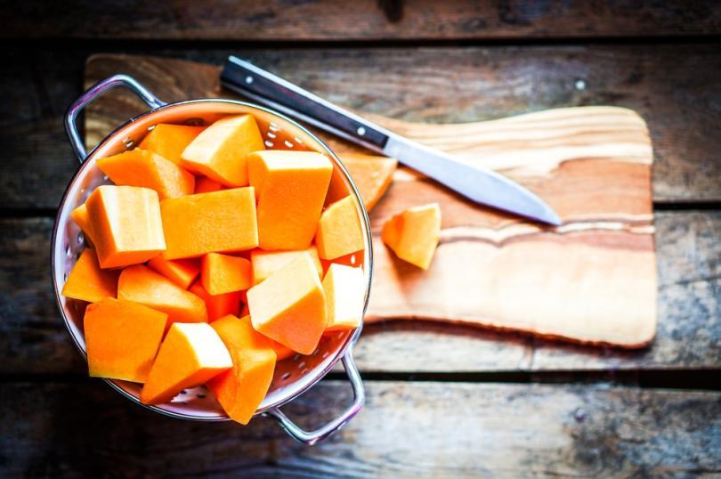 Chopped pumpkin in a sieve on chopping board with a knife lying next to it.