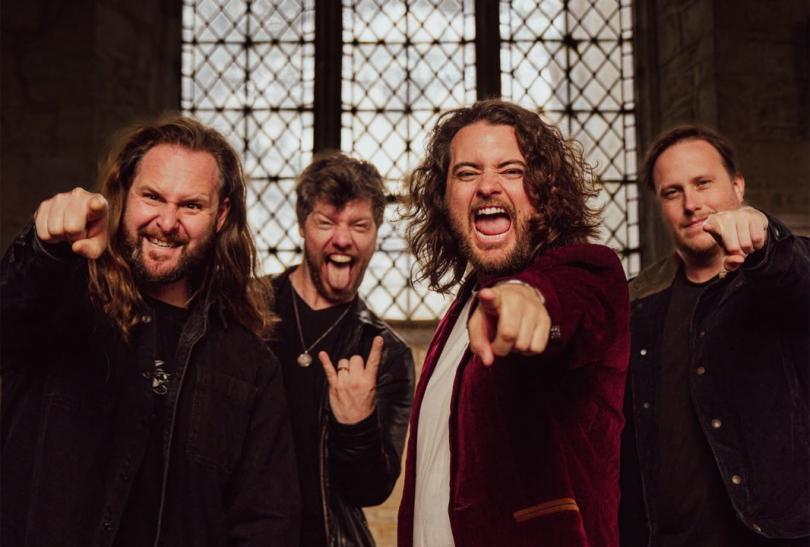 Four members of the band making a screaming expression and pointing at the camera