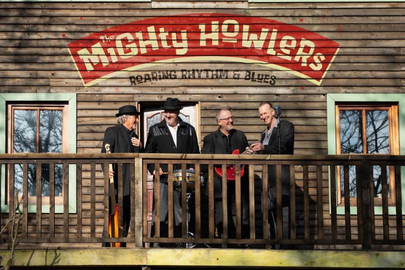 The Mighty Howlers band members standing outside a wooden shack