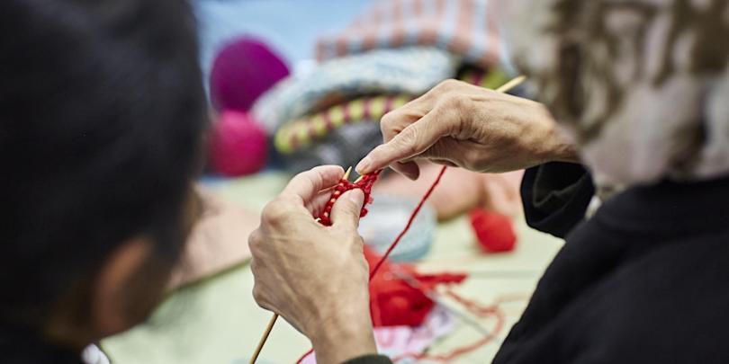 A close up of hands knitting with red yarn