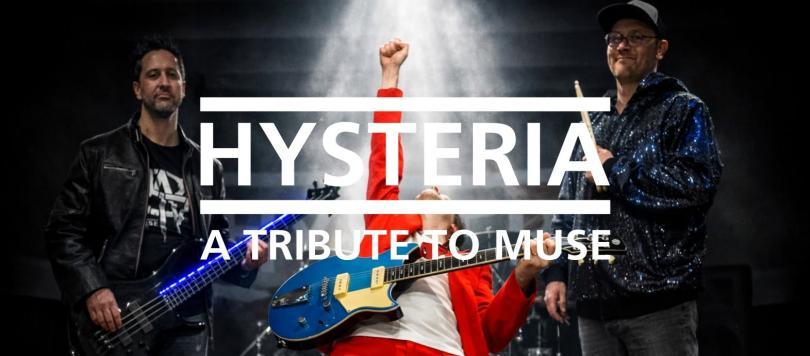 Three band members standing around - the lead guitarist in the middle is leaning back with his fist in the air
