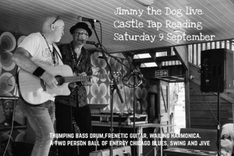 Black and white image of two white-skinned older male musicians standing behind mics on the left of the picture. The slightly nearer person is holding a guitar. The ceiling is low and the wallpaper behind them looks like 70s kitsch.