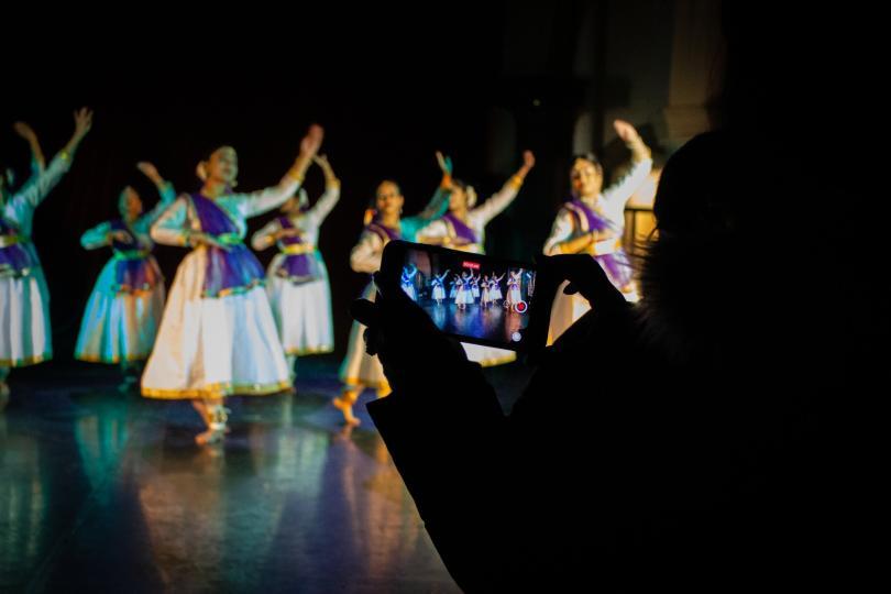 South Asian dancers on a stage with a mobile phone taking a photo of them