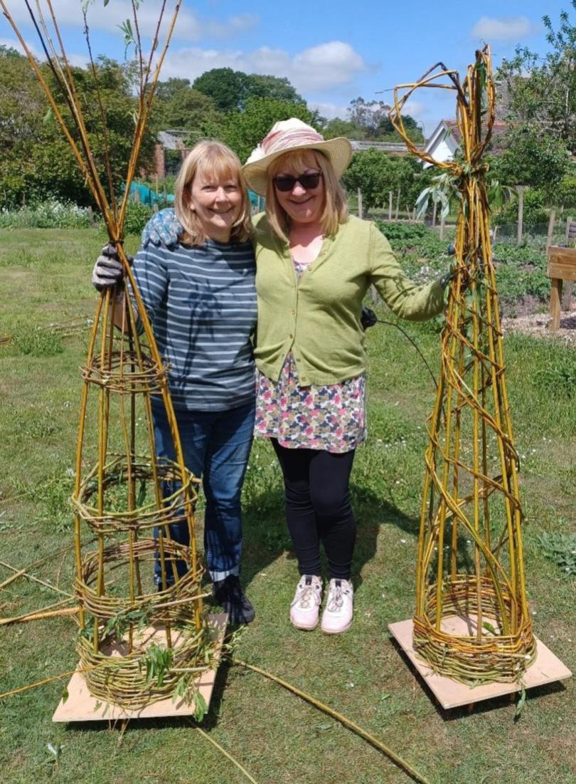 Two women in gardning clothes, each holding a willow obelisk