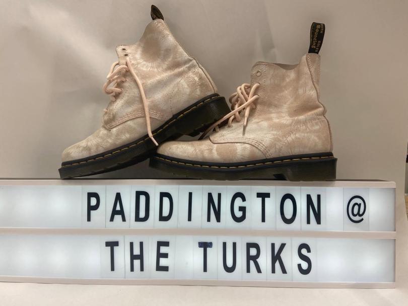 A pair of white Doc Martens over a sign saying "Paddington @ the Turks"