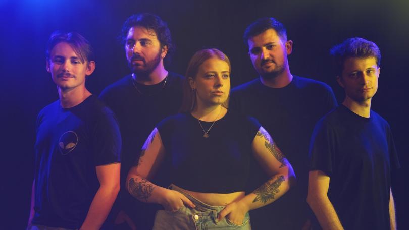 Five band members standing under purple lights