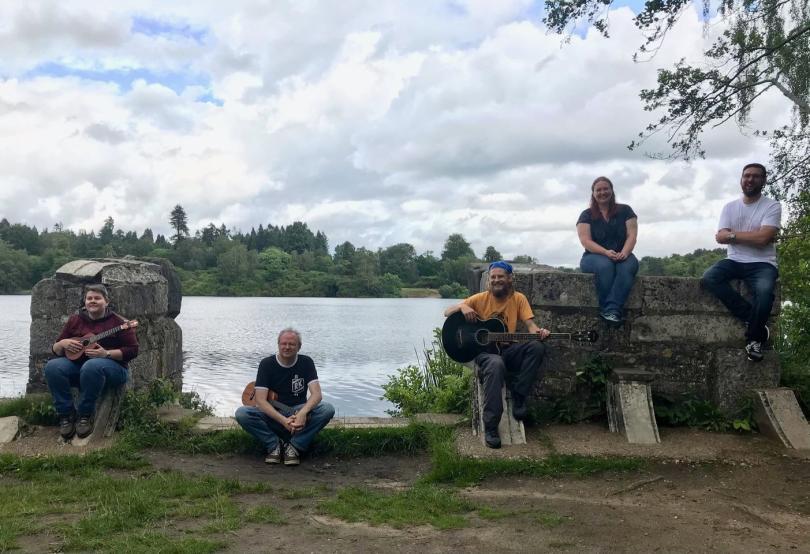 Miscellaneous musicians with their instruments sitting on some old walls by a large body of water