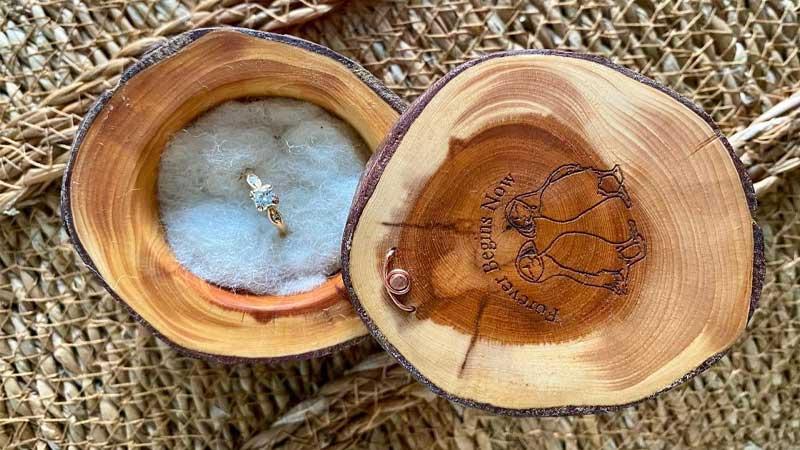 Yew ring box with white felted insert and engraved lid holding an engagement ring.