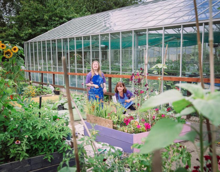 Two people gardening in front of a greenhouse