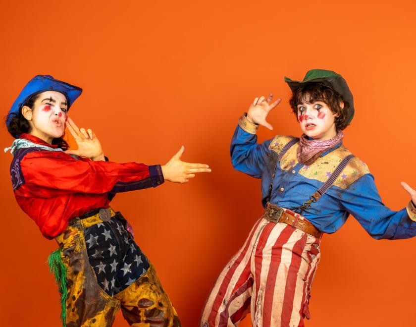 Actor-performers Xhloe and Natasha dressed as rodeo clowns and pulling finger guns on each other