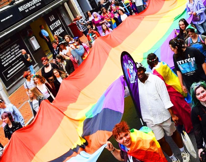 Reading Pride parade going down Friar Street, with a group of people carrying a massive rainbow flag