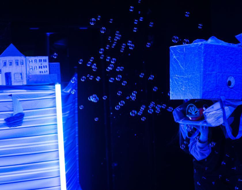 Photo of a performer holding a large handheld prop shaped like a whale, blowing bubbles from its mouth
