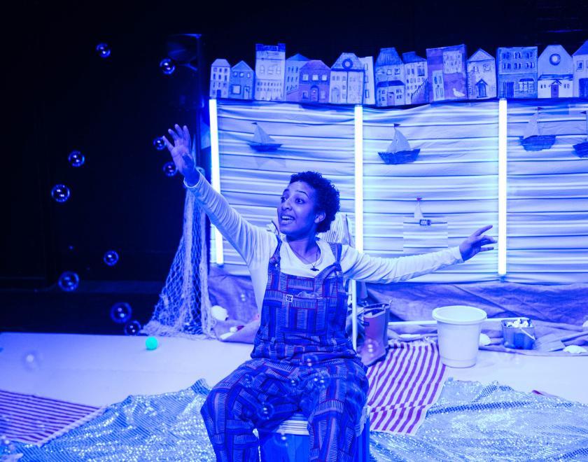 Photo of the lead performer sitting in the centre of the set bathed in blue light.