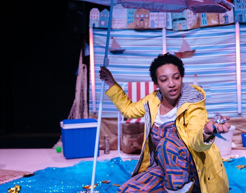 Photo of the lead performer crouching beneath a beach umbrella