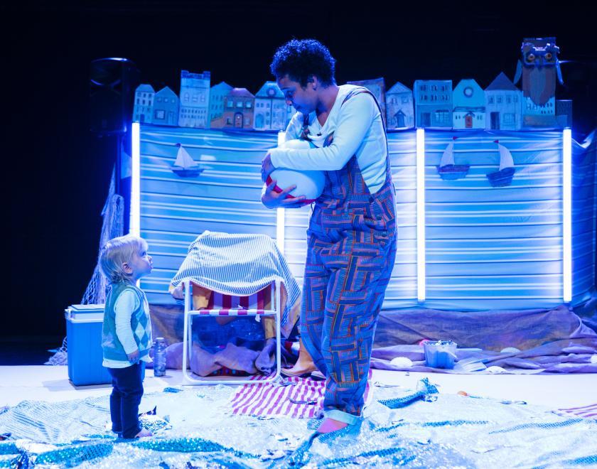 Photo of the lead performer on stage with a toddler, the performer is holding a beach ball