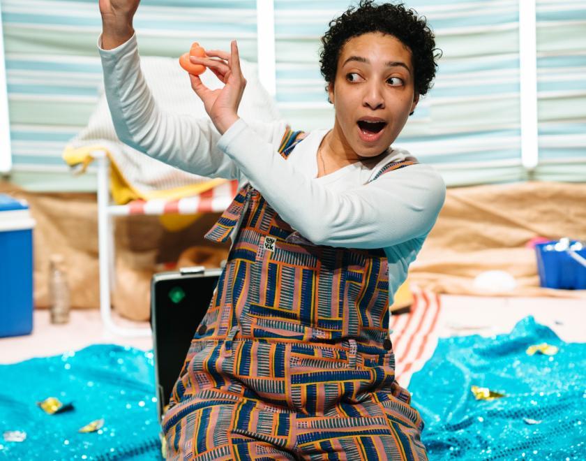Photo of the lead performer kneeling on stage holding up two small rubber ducks