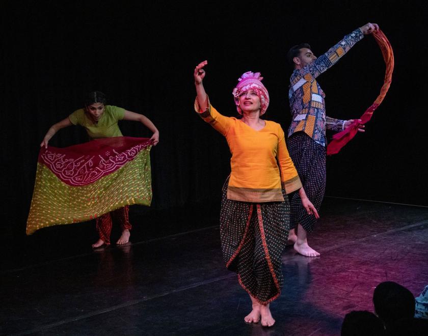 Three performers wearing brightly coloured clothes and dancing with colourful scarves.